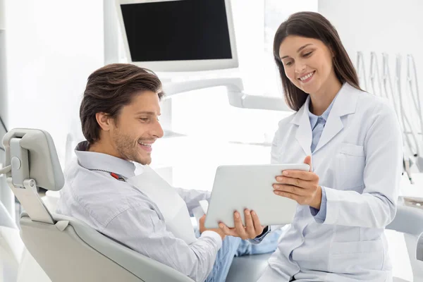 Odontólogo alegre que muestra los resultados del tratamiento en la tableta digital — Foto de Stock