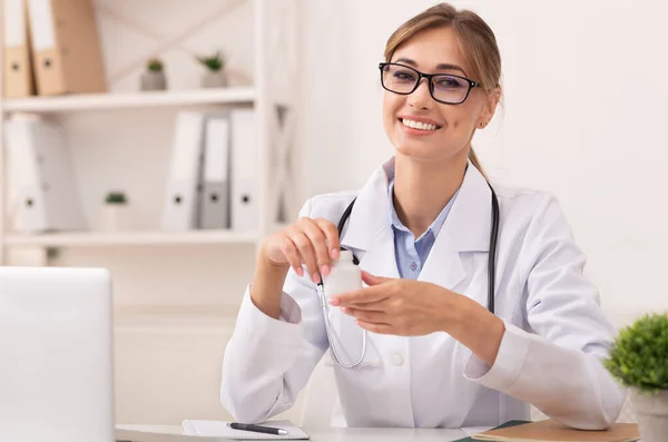 Χαμογελώντας γιατρός γυναίκα κρατώντας συνταγογραφούμενα φάρμακα Jar κάθεται στο γραφείο — Φωτογραφία Αρχείου