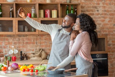 Mutlu evli çift mutfaktaki akıllı telefondan selfie çekiyor.