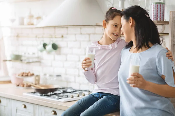 Joven madre soltera e hija bebiendo leche en la cocina juntos —  Fotos de Stock