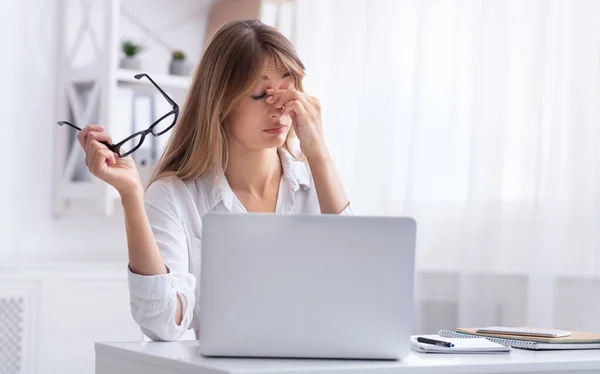 Přepracovaná dívka masáže Nosebridge sedí na notebooku na pracovišti — Stock fotografie