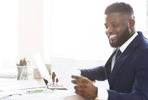 Hombre de negocios negro satisfecho revisando informes, sentado en la oficina moderna — Foto de Stock