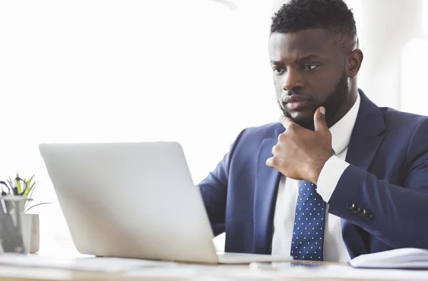 Pensativo afroamericano joven que trabaja con el ordenador portátil en la oficina —  Fotos de Stock
