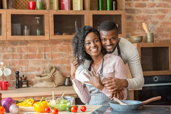 Alegre hombre negro abrazando a su esposa mientras cocina en la cocina — Foto de Stock
