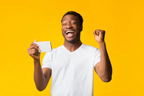 Afro-Mann hält Smartphone mit zitternden Fäusten vor gelbem Hintergrund — Stockfoto