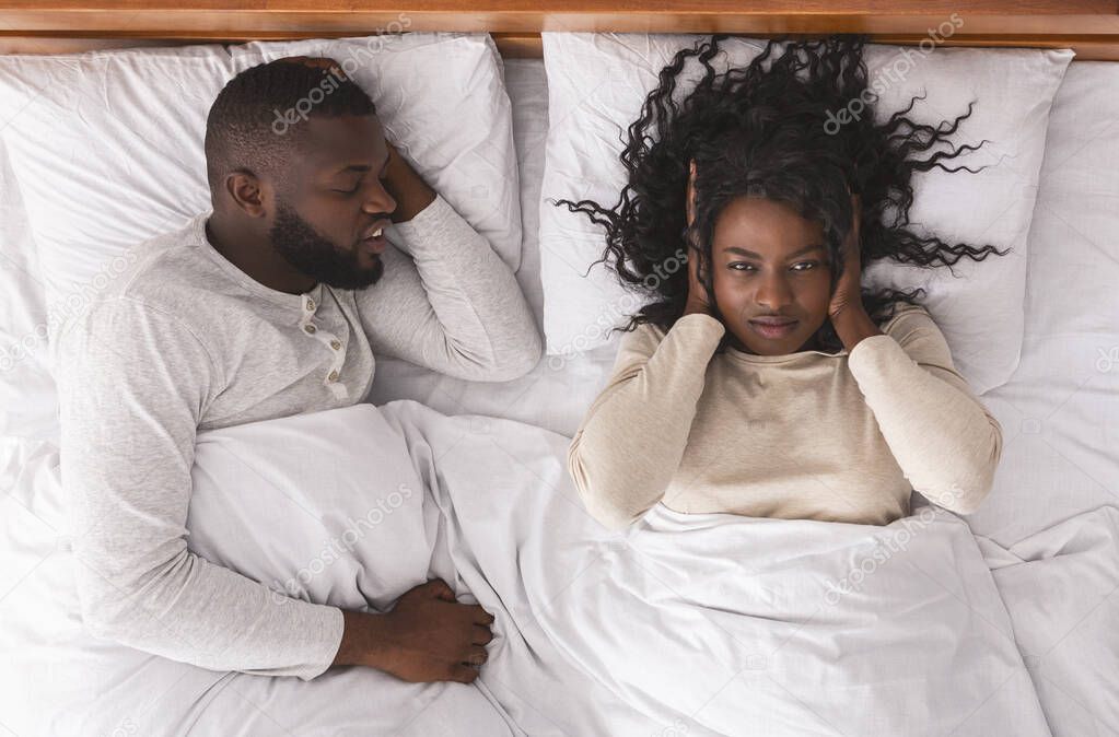 Black woman closing ears tired of her husbands noisy snoring.