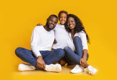 Üç kişilik Afro milenyum ailesi yerde oturup birbirlerine sarılıyorlar.