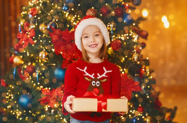 Niña de pie junto al árbol de Navidad sosteniendo su regalo —  Fotos de Stock