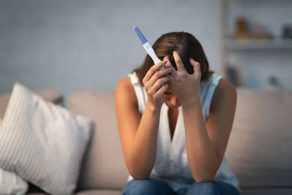 Zoufalá žena drží těhotenský test sedí na pohovce doma — Stock fotografie