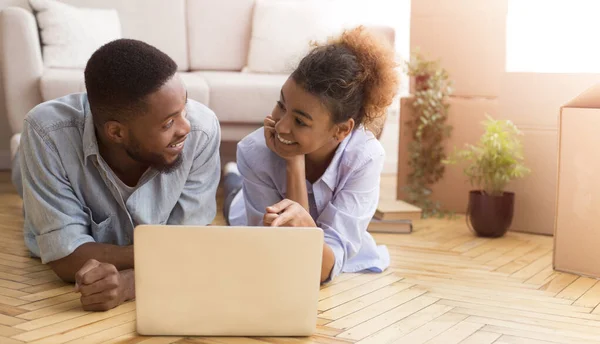 Couple afro utilisant ordinateur portable allongé sur le sol dans une nouvelle maison — Photo