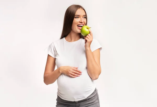 妊娠中の女性が白いスタジオの背景にAppleのポーズを食べる — ストック写真