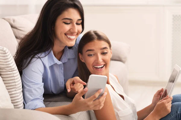 Две девушки с телефоном и планшетом сидят на диване в помещении — стоковое фото