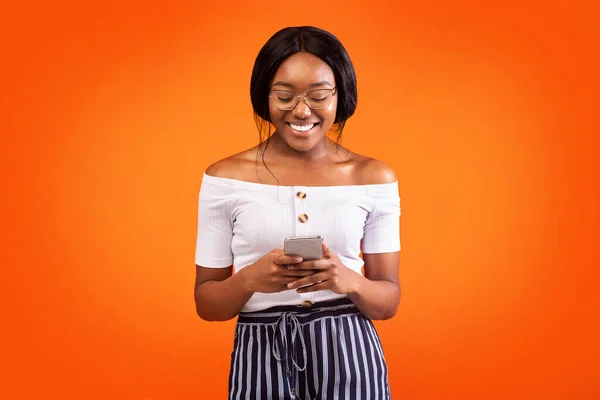 Usmívající se černá dáma stojící pomocí smartphonu a chatování, Studio Shot — Stock fotografie