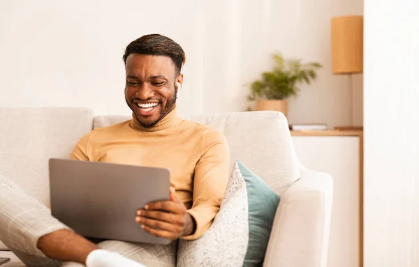 Hombre alegre usando el ordenador portátil viendo la película sentado en el sofá interior — Foto de Stock