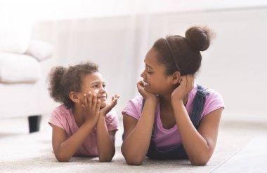 Afro kız kardeşler yerde yatar ve birbirlerine gülümserler.
