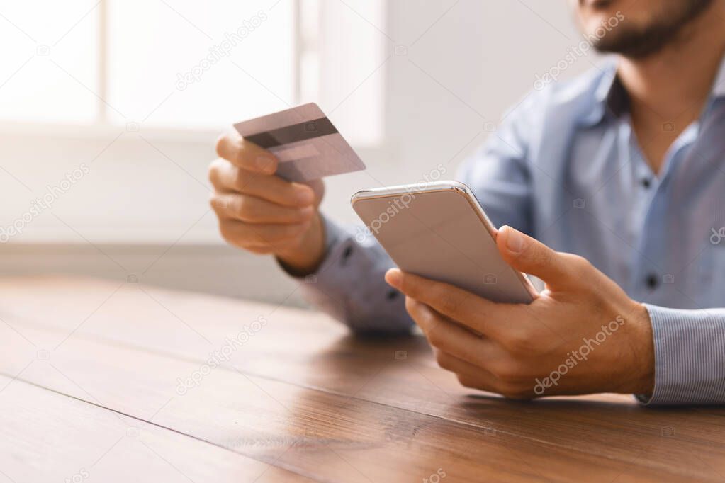 Unrecognizable man using smartphone and credit card, purchasing goods online