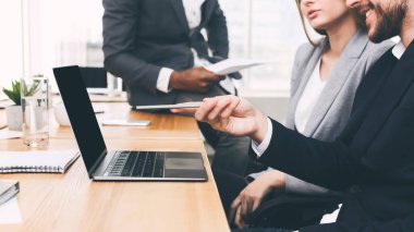 Meslektaşlar yeni projeyi tartışıyor, dizüstü bilgisayarı işaret ediyor