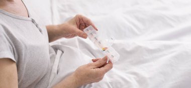 Yaşlı kadın yatakta hap kutusundan ilaç alıyor.