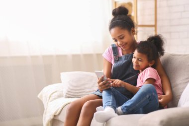 Neşeli Afrikalı kız kardeşler evde cep telefonu kullanıyor.