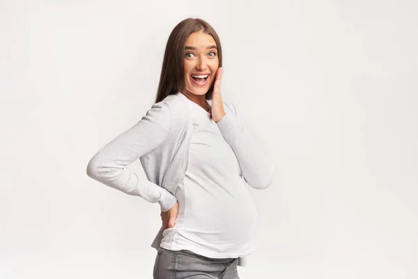 Opgewonden zwangere vrouw aanraken kin glimlachen bij de camera, Studio Shot — Stockfoto