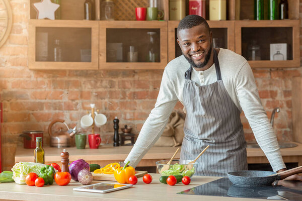 Attractive black man posing at kitchen while cooking