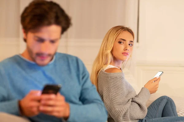 Esposa viendo a marido enviando mensajes de texto en el teléfono sospechando infidelidad sentado en el interior —  Fotos de Stock