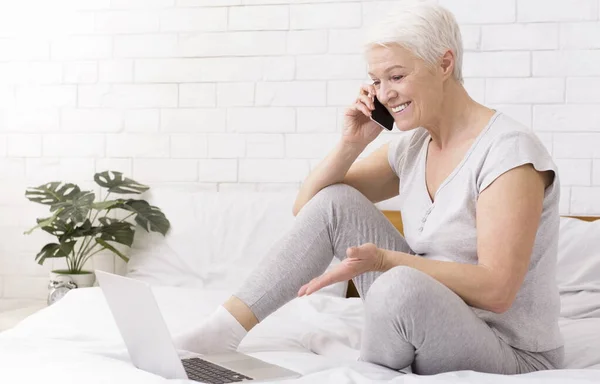 Positive senior businesswoman working on laptop and talking on phone
