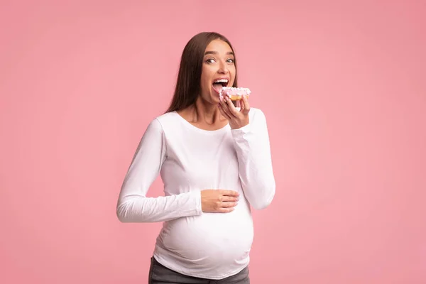 Wanita hamil Memakan Donut Di Latar Belakang Merah Muda, Studio Ditembak — Stok Foto