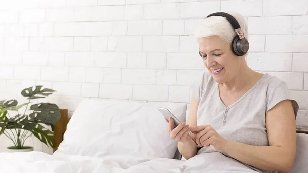 Ηλικιωμένη γυναίκα που ακούει μουσική στο κινητό στο κρεβάτι — Φωτογραφία Αρχείου