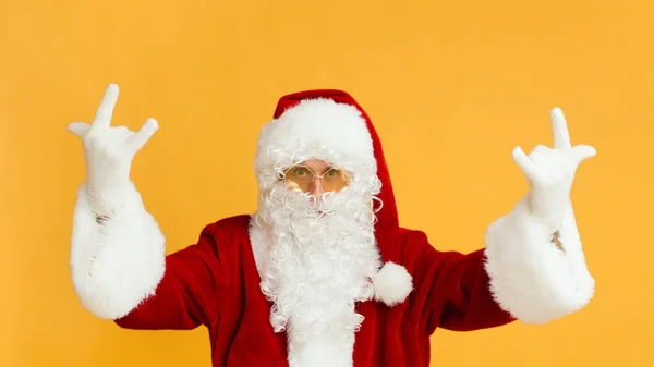 Man in Santa costume and yellow glasses showing horn sign — Stock Photo, Image
