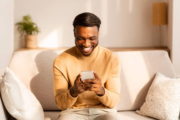 Hombre feliz usando mensajes de texto Smatphone sentado en el sofá en casa — Foto de Stock