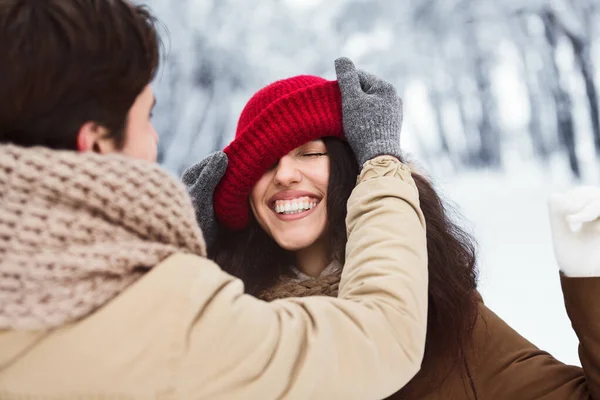 Älskande pojkvän sätta Cap på flickvännen stående i snöig skog — Stockfoto