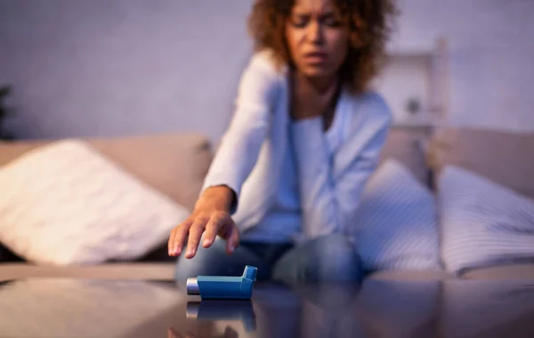 Asthma attack. Young woman reaching inhaler on table