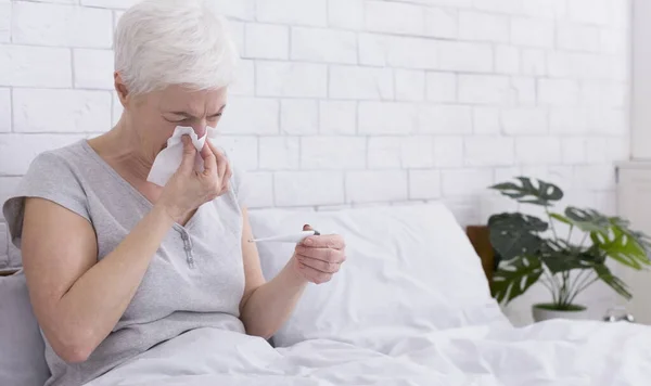 Enferma señora mayor midiendo la temperatura corporal, sonando la nariz en la cama — Foto de Stock