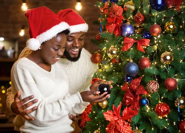 Noel Baba şapkalı Afrikalı çift Noel ağacını süslüyorlar. — Stok fotoğraf