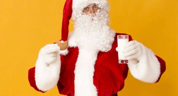 Weihnachtsmann isst Kekse und trinkt Milch auf orangefarbenem Hintergrund — Stockfoto