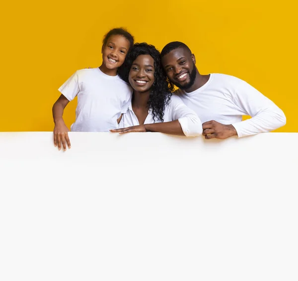 Família afro feliz inclinando-se na placa branca em branco para propaganda — Fotografia de Stock