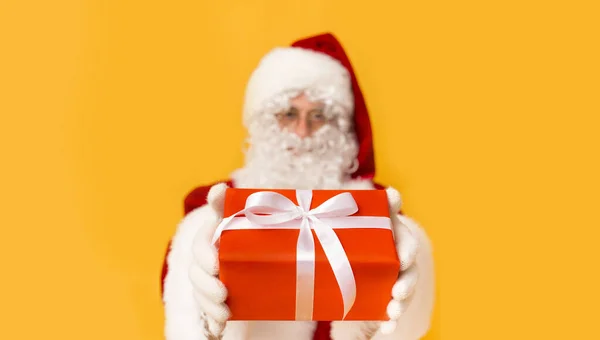 Schöner Weihnachtsmann schenkt dir ein Geschenk in roter Schachtel auf orange — Stockfoto