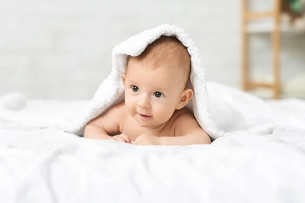 Adorable newborn boy lying on bed under soft white blanket