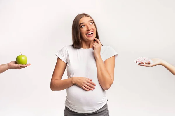妊娠中の女性は、アップルとドーナツ立ちの間で選択,スタジオショット — ストック写真