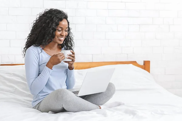 Beautiful smiling young woman watching movie on laptop, drinking tea