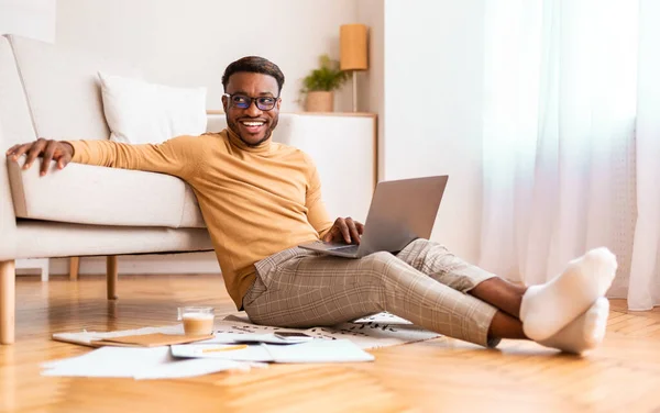在笔记本电脑上工作的非洲人坐在家里的地板上 — 图库照片