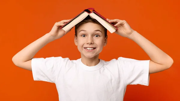 Wesoły nastolatek ukrywający się pod książkowym dachem — Zdjęcie stockowe