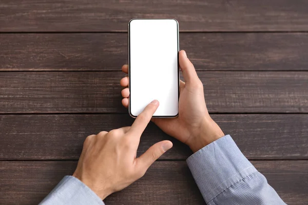 Чоловічі руки торкаються смартфона з порожнім екраном на дерев'яному фоні — стокове фото
