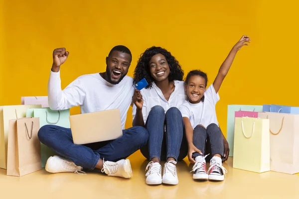 Gelukkig zwart gezin met laptop, creditcard en boodschappentassen. — Stockfoto