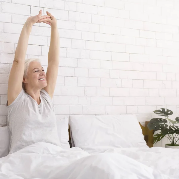 Cheerful well-slept senior lady stretching in bed in morning — Stock Photo, Image