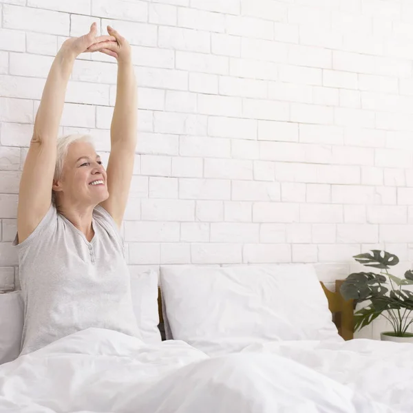 Alegre señora mayor bien dormida estirándose en la cama por la mañana —  Fotos de Stock