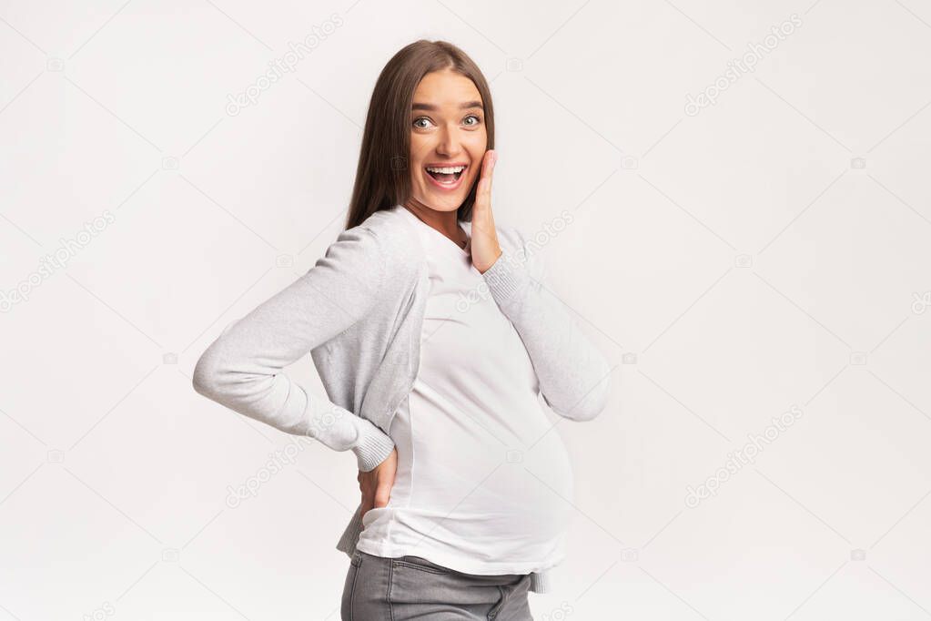 Excited Pregnant Woman Touching Chin Smiling At Camera, Studio Shot