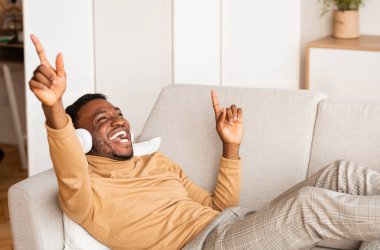 Kulaklıklı Afro Adam müzik dinliyor ve evde şarkı söylüyor.