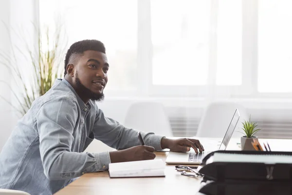 Hombre negro tomando notas de la computadora portátil en el lugar de trabajo en la oficina — Foto de Stock